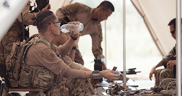 Group of soldiers inside an army tent, one drinking water